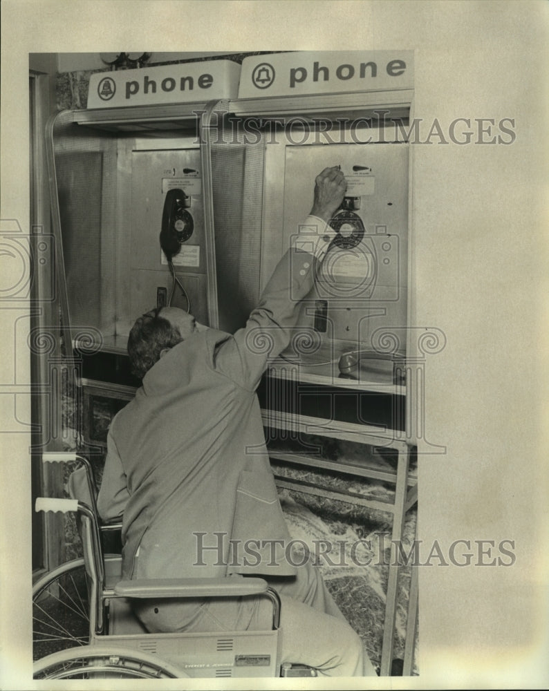 1976 Person in a wheelchair reaches for telephone - Historic Images