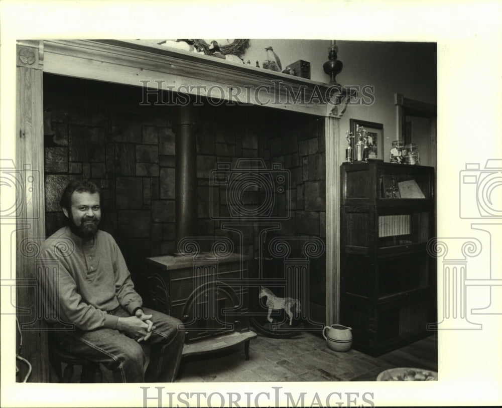 1988 Press Photo Dennis Hinds, Covington resident, sitting beside a wood stove - Historic Images