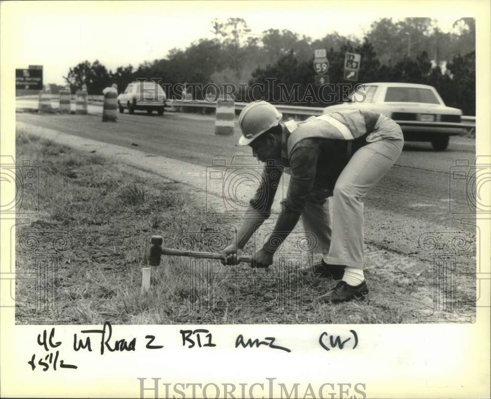 1989 Press Photo Burnell Dudley hammers stake into ground on Interstate 12 - Historic Images