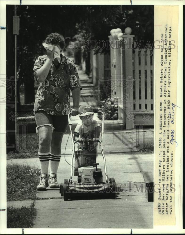 1988 Wanda Hebert wipes face while son Wilbert helps push lawnmower - Historic Images