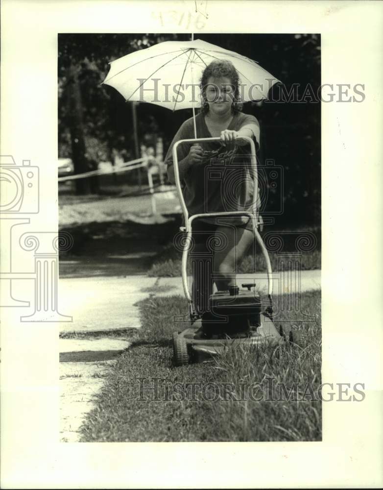 1986 Press Photo Stacey Sivori cutting grass on Bonnabel Blvd with an umbrella - Historic Images