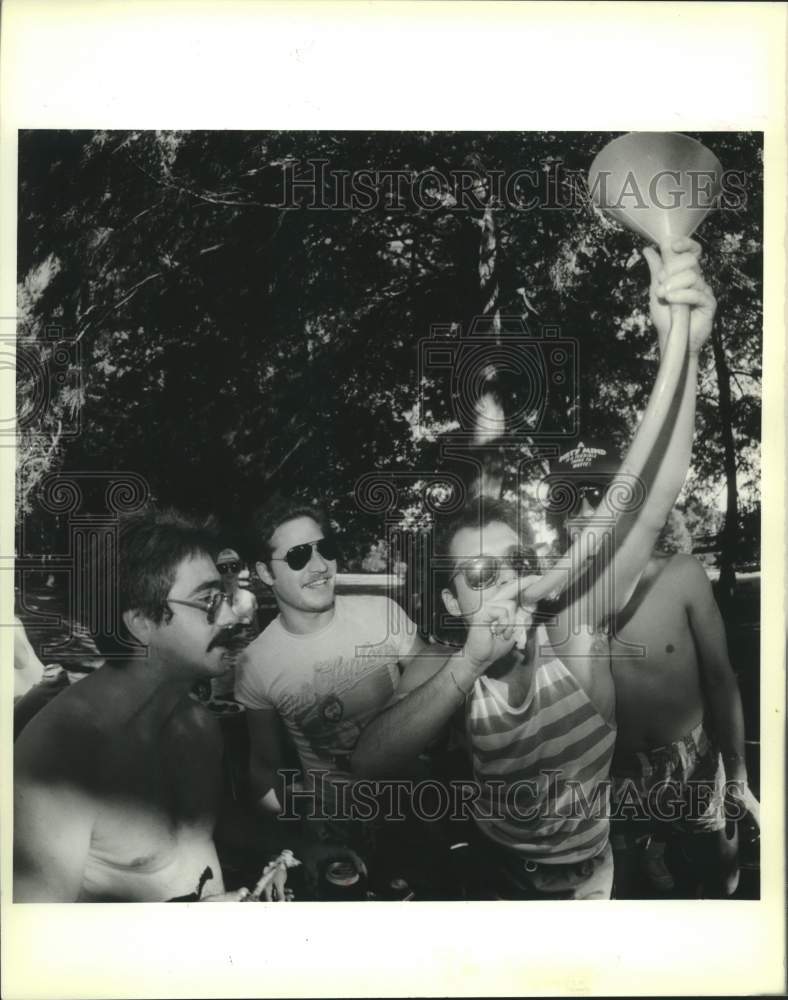 1988 Press Photo George Sens uses funnel to down two beers as his friends cheer. - Historic Images