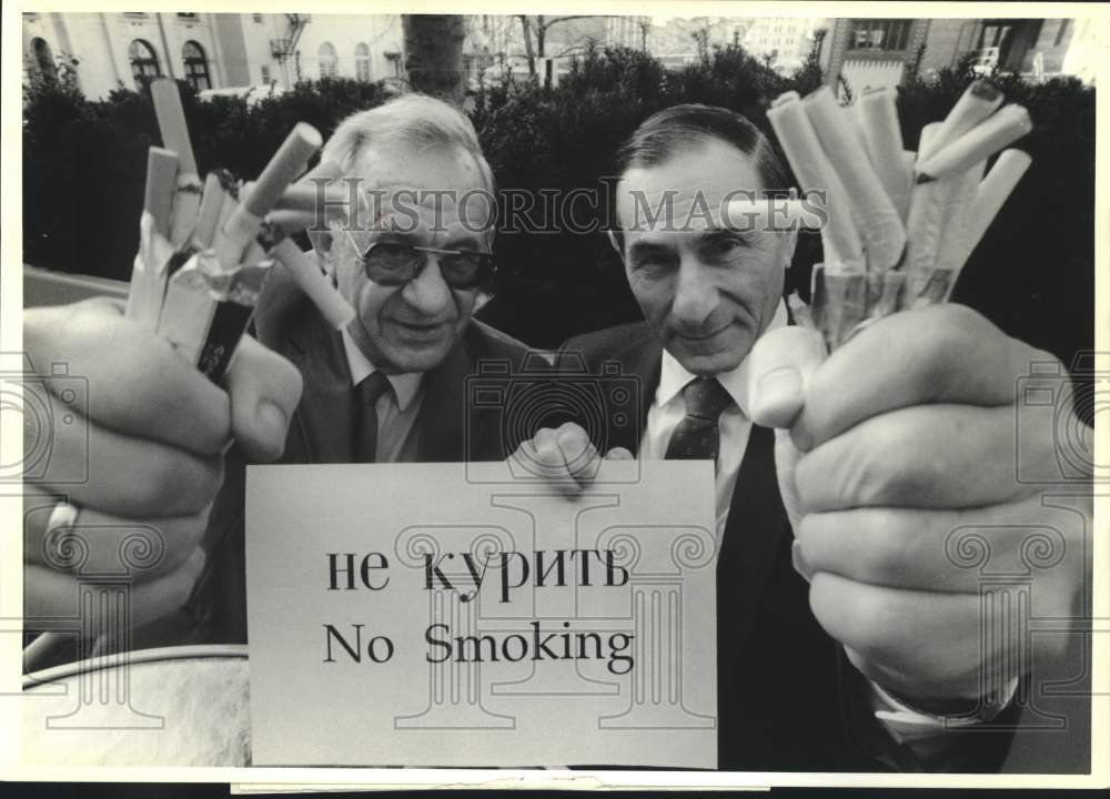 1989 Press Photo Dr. Yuri Lupukhin &amp; Dr. Gus Miller grasp fistful of cigarettes - Historic Images