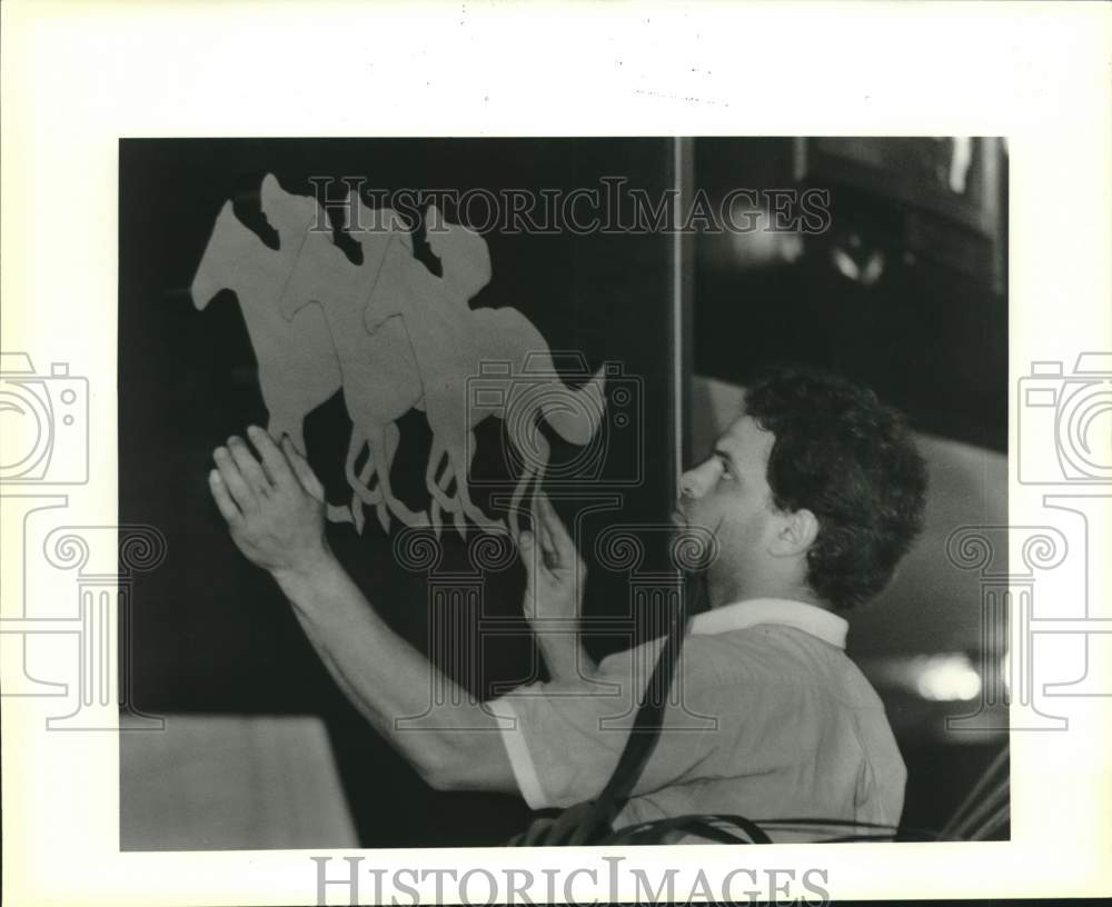 1989 Press Photo David Borrello adjusts a wall hanging of race horses in Arabi- Historic Images