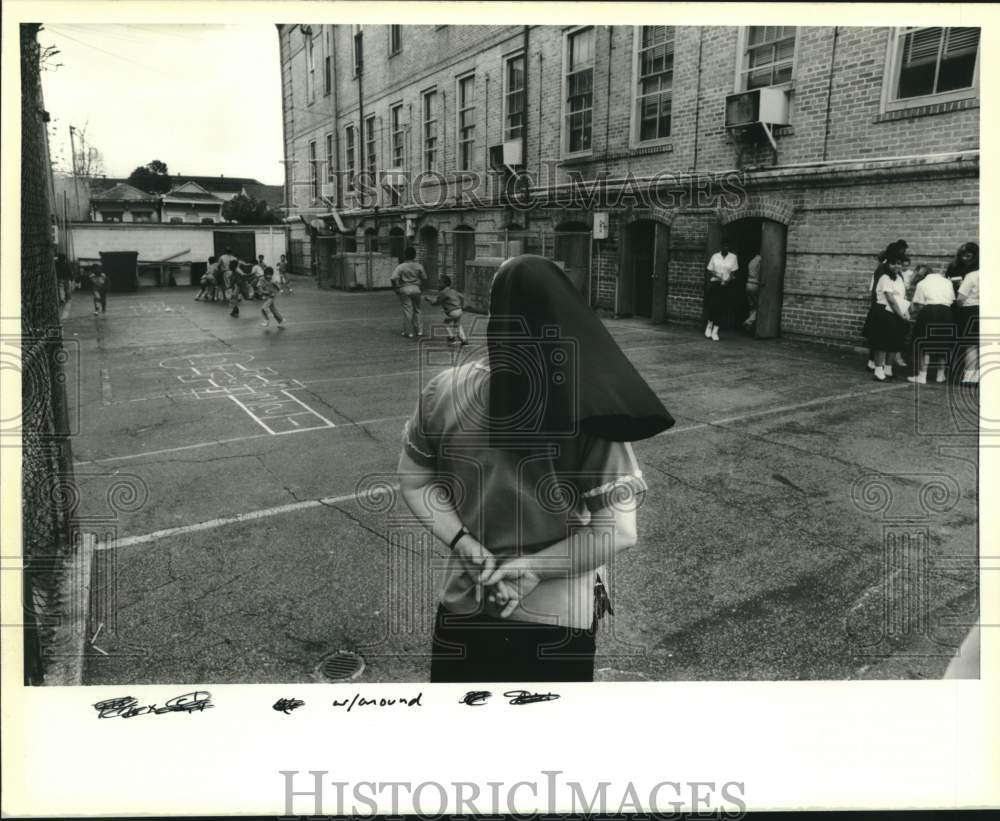 1990 Principal watches kids at recess at Saints Peter &amp; Paul school - Historic Images