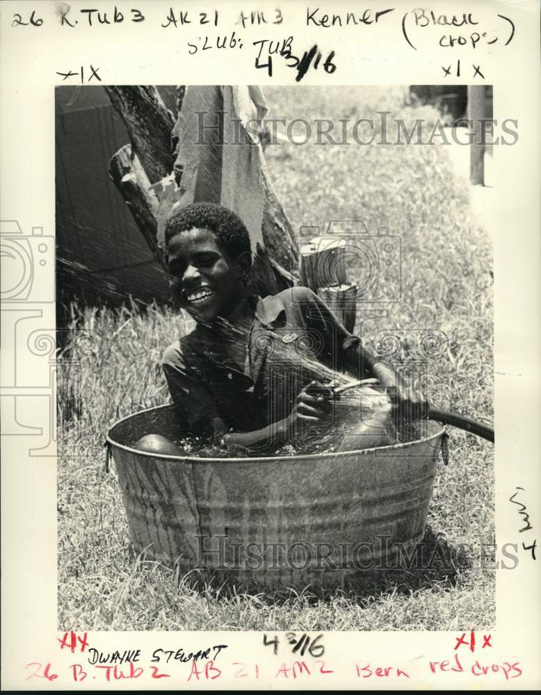 1985 Dwayne Stewart keeps cool by garden hose and wash tub - Historic Images