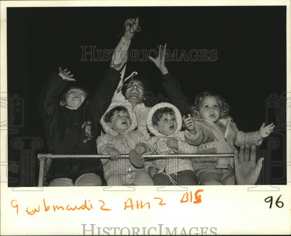 1983 Frank Cambas reaches for beads over his daughters on Mardi Gras - Historic Images