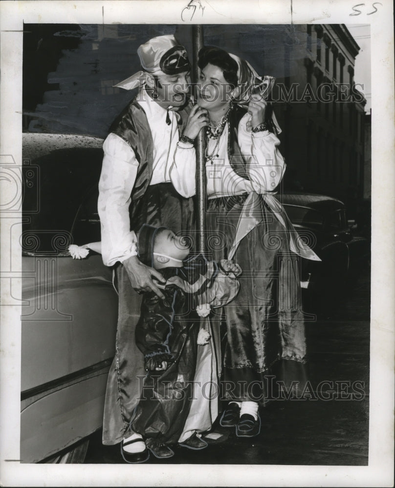 1955 costume family standing around a street pole at Mardi Gras - Historic Images
