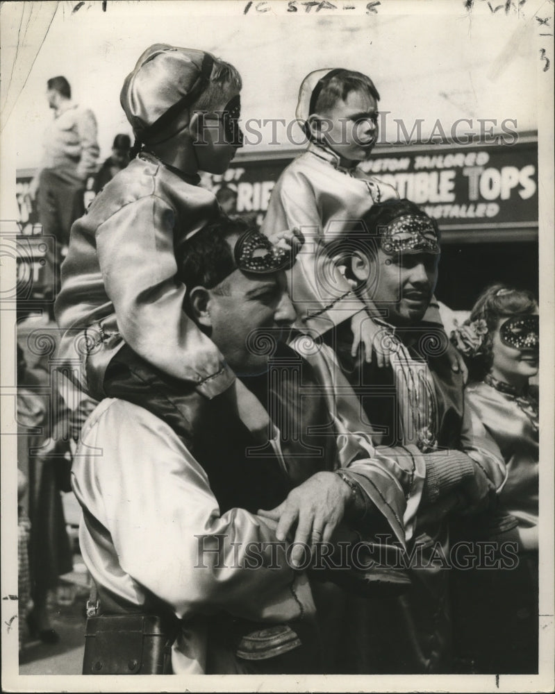 1954 Costumed kids ride on shoulders for better views at Mardi Gras - Historic Images
