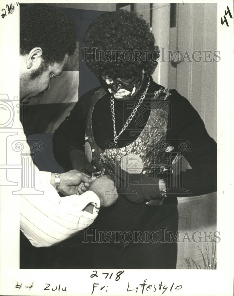 1981 Carnival Parade King of Zulu gets royal armor adjusted. - Historic Images