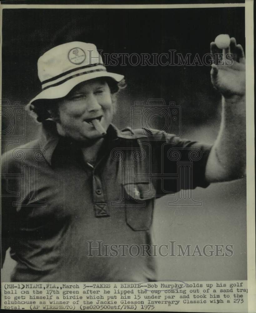 1975 Press Photo Golfer Bob Murphy, with cigar in mouth, holds up his golf ball - Historic Images