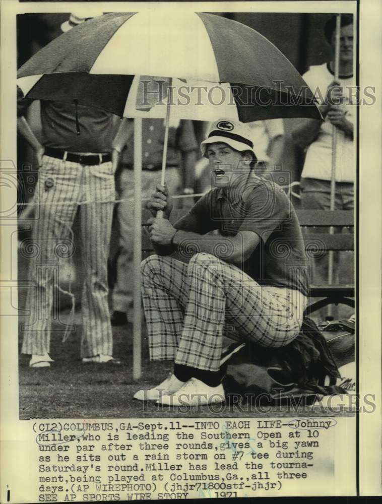 1971 Press Photo Golfer Johnny Miller sits on his golf bag holding an umbrella - Historic Images