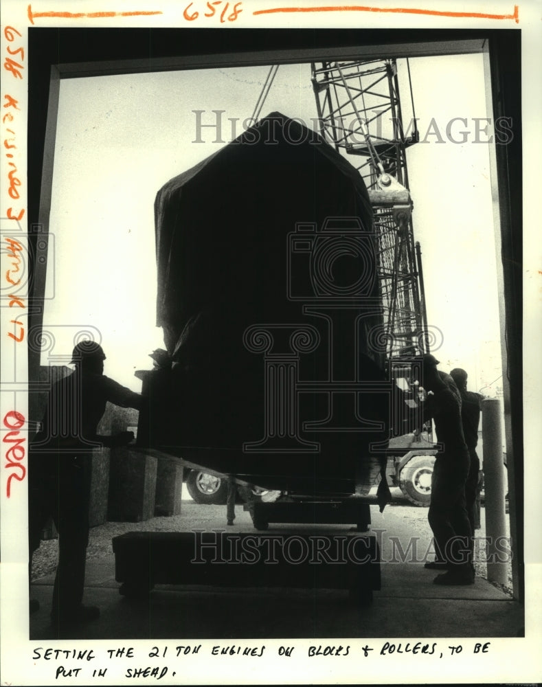 1983 Cranes unload two diesel engines at a warehouse; set on blocks - Historic Images