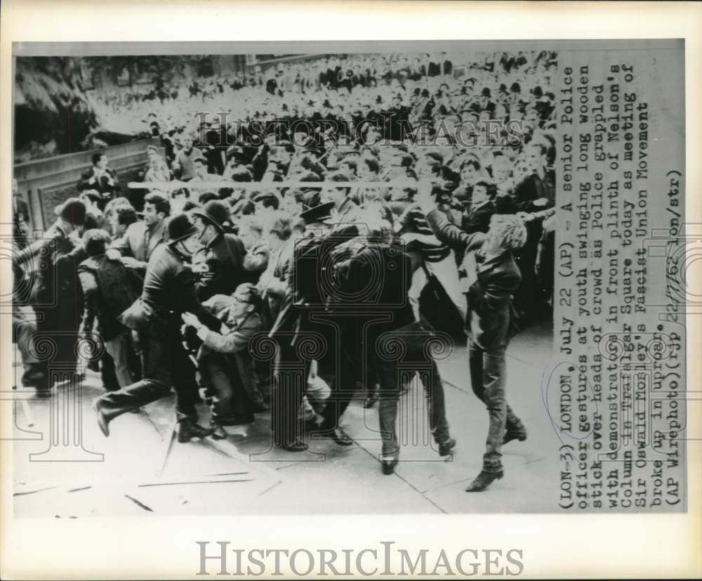 1962 Policeman gestures at youth swinging wooden stick over crowd - Historic Images