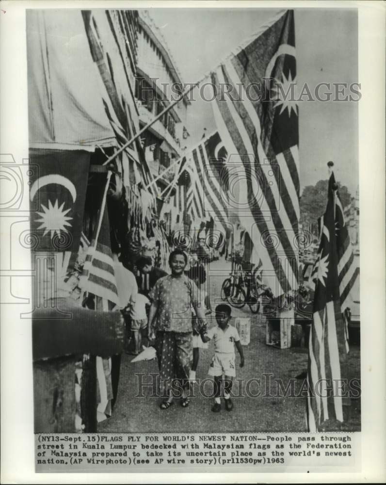 1963 People walk street in Kuala Lumpur with Malaysian flags flying - Historic Images