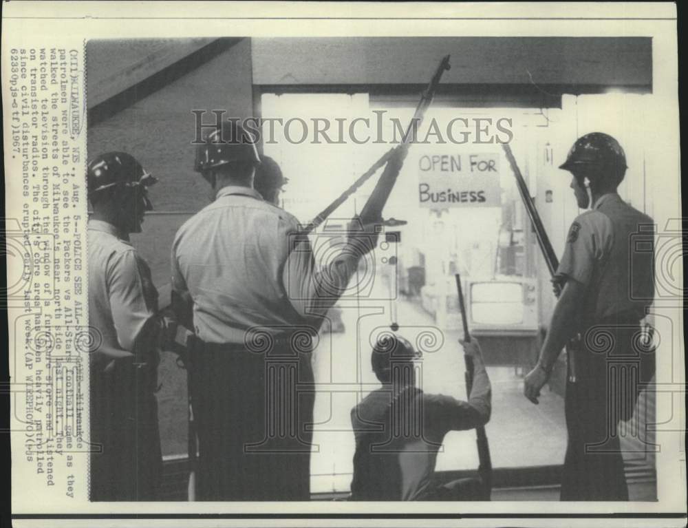 1967 Milwaukee patrolmen watch football game while patrolling street - Historic Images