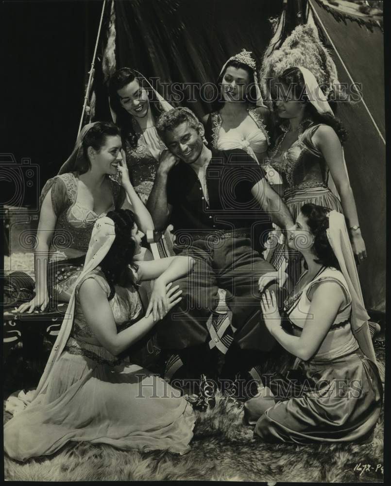 Actor Jeff Chandler surrounded by a harem of women in movie scene - Historic Images