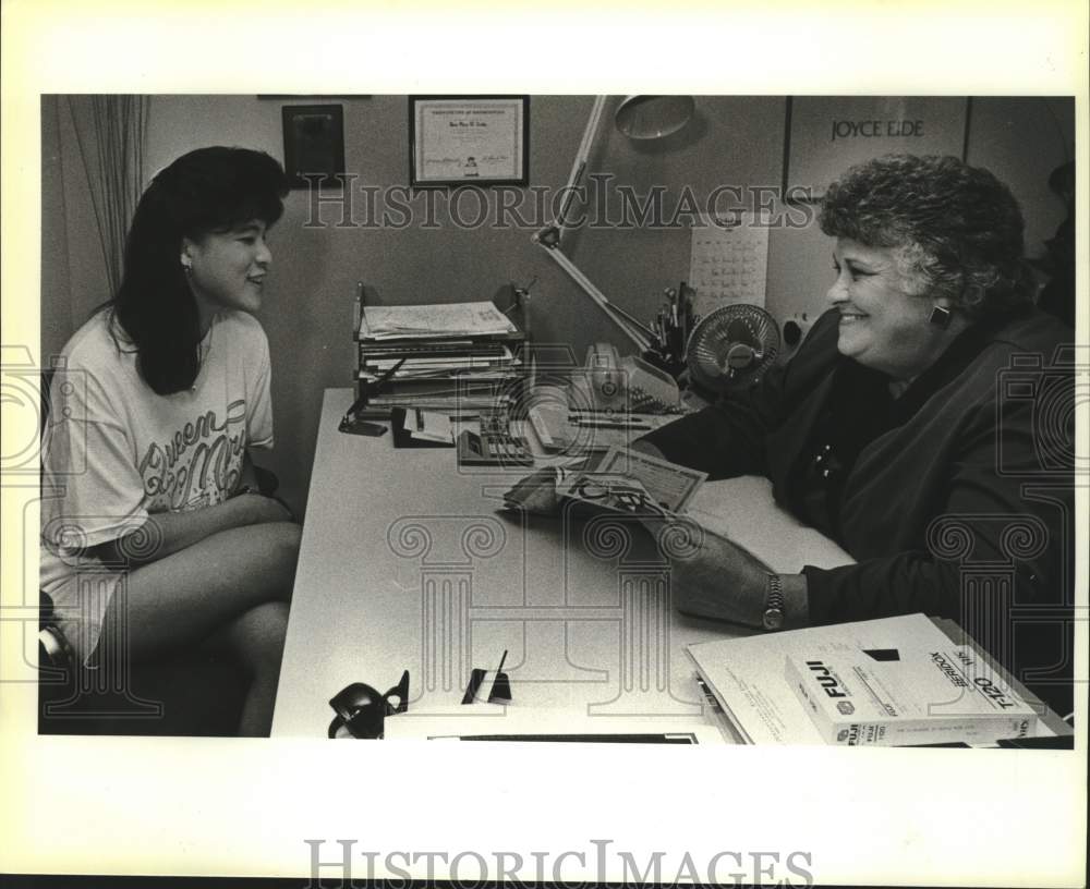 Rosemary Droke sits at desk smiling at young girl on other side - Historic Images