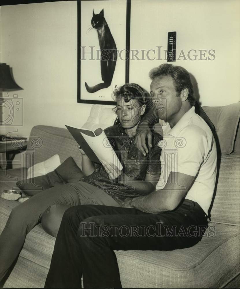 Guy Eevsyrn leans on shoulder of woman reading on couch - Historic Images