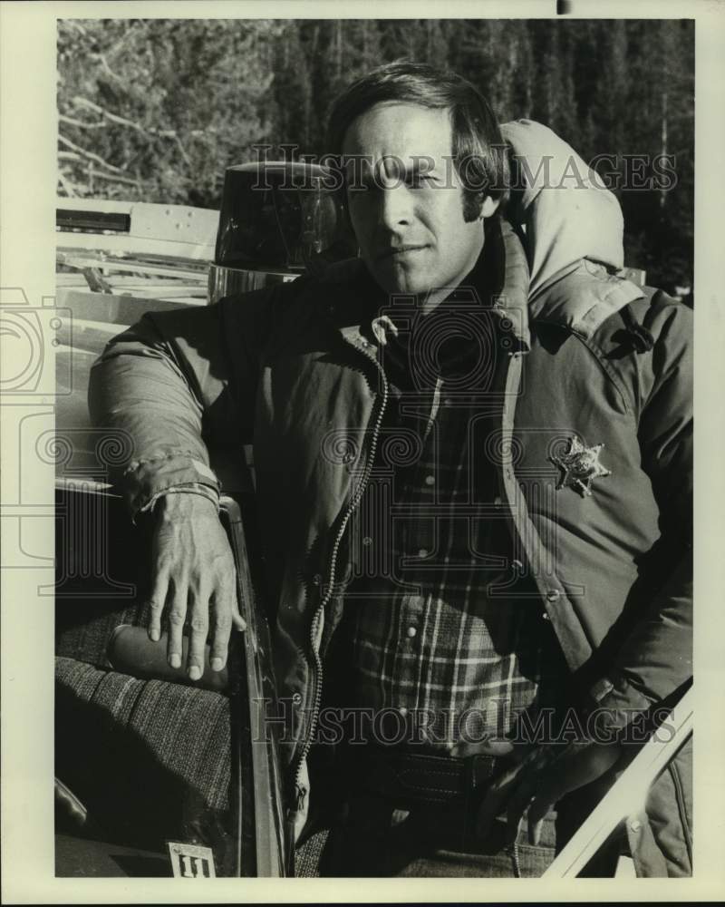 Press Photo Actor Portrays Police Officer in Parka, Leans on Cruiser - Historic Images