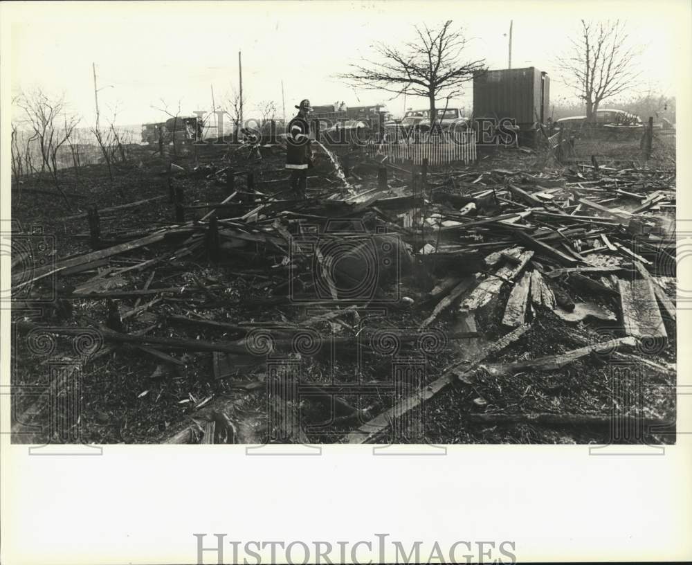 1987 Press Photo Firefighter hosing down smoldering fire debris - Historic Images