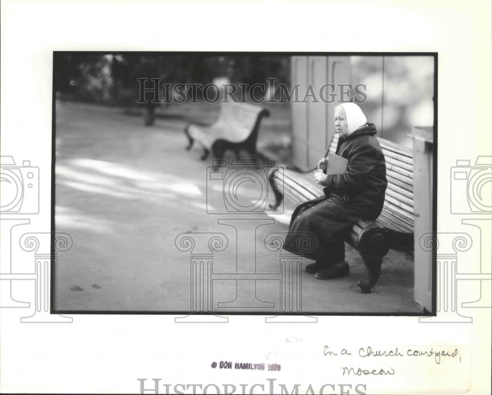 1989 Press Photo An old lady sits on a bench in a church courtyard, Moscow - Historic Images