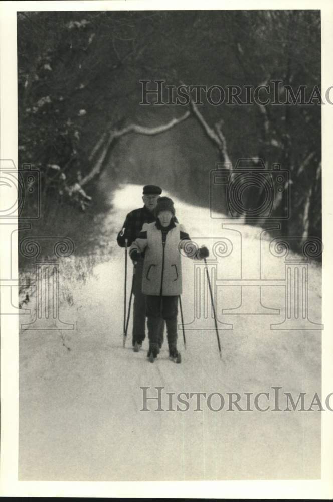 1987 Press Photo Older Man and Woman Skiing down Snow covered Road - sya61538 - Historic Images