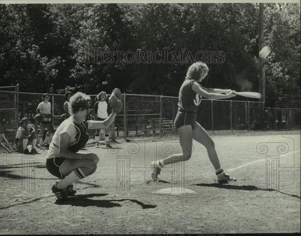 Press Photo Girl swinging at ball and catcher behind her at softball game - Historic Images