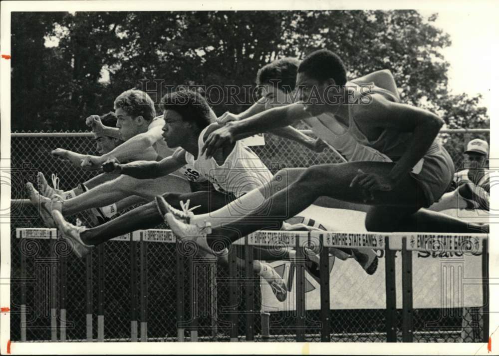 1984 Press Photo Men's track athletes leap over hurdle in close heat- Historic Images