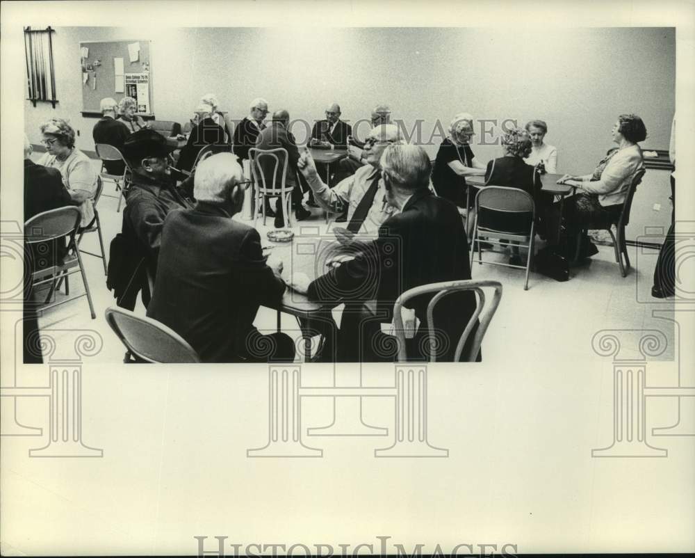 Senior citizens fill tables in room playing cards and laughing - Historic Images