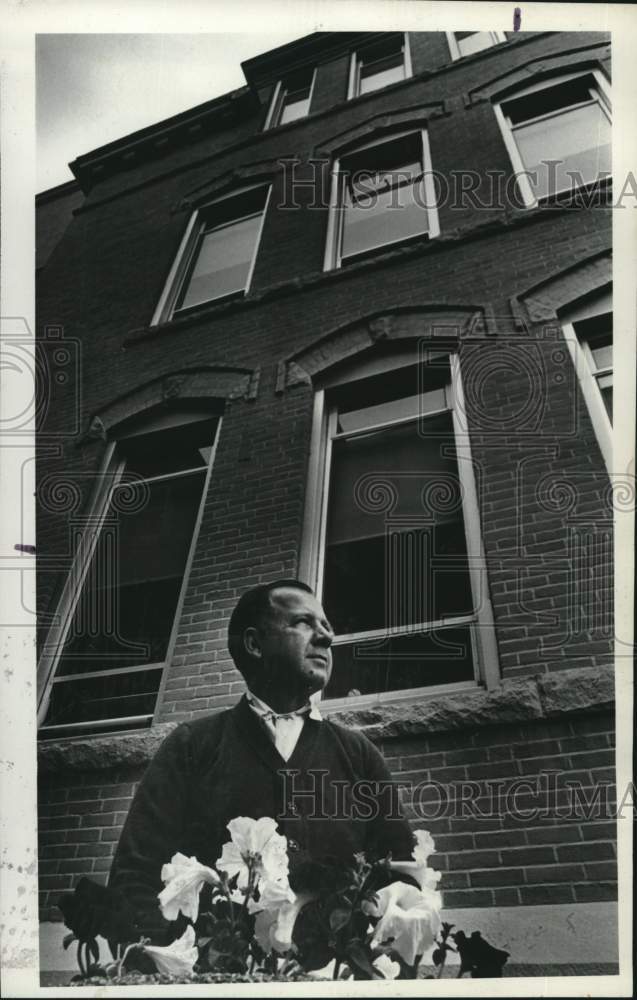 1974 George Loskowitz stands outside a building looking at flowers - Historic Images