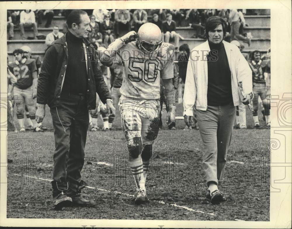 Press Photo Mud covered #50 football player is walked off the field by coaches - Historic Images