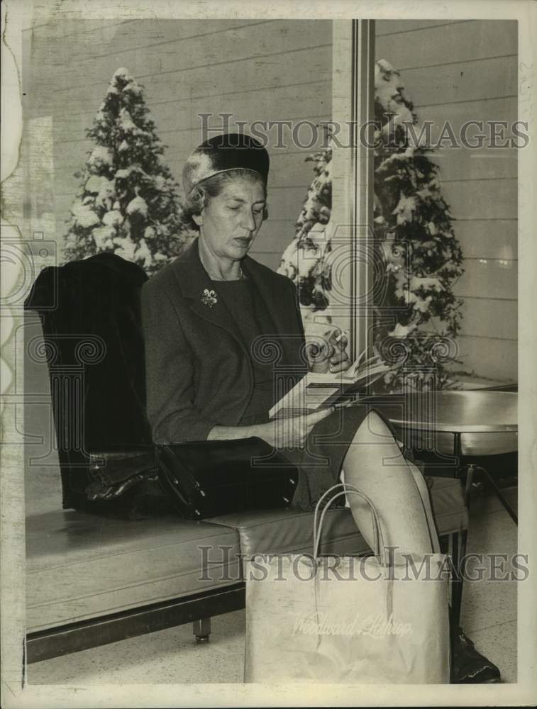 1963 Mrs. Charles Batters reads book at Albany Airport, New York - Historic Images