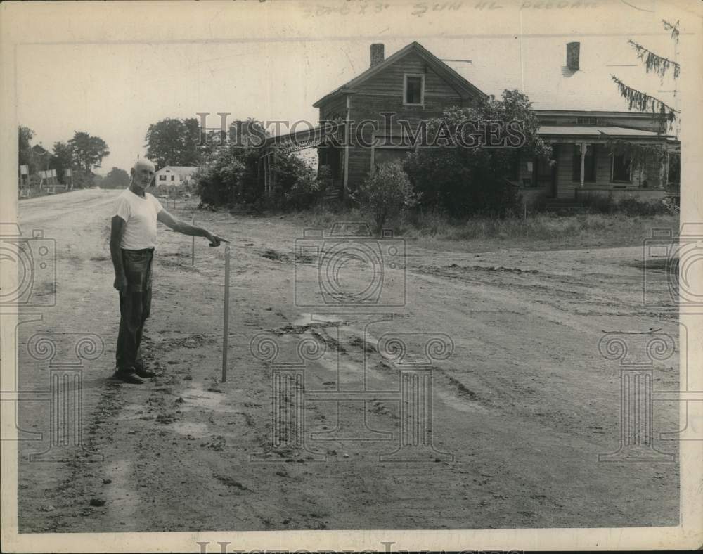 1963 A man points at a stake near a house and road-Historic Images