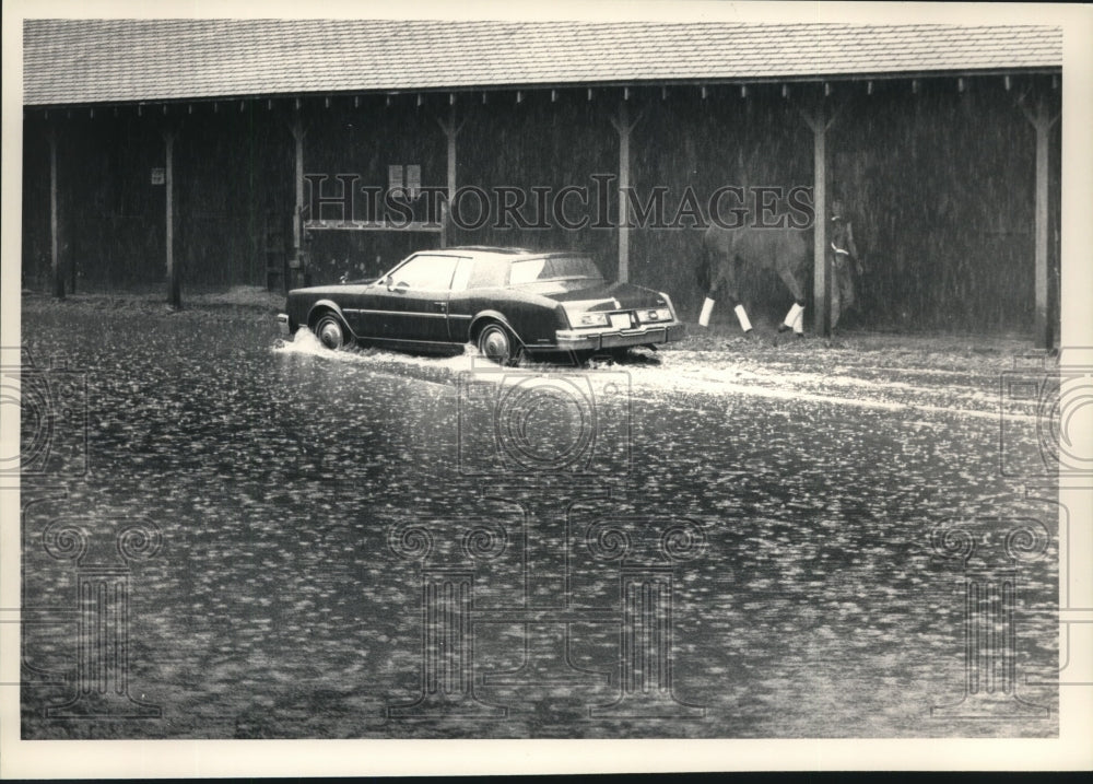 1988 Press Photo Car drives through a mini lake alongside barn 9 at Saratoga- Historic Images